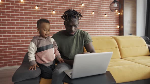 Father and Small Boy Typing Together on Laptop at Home on Sofa Slow Motion