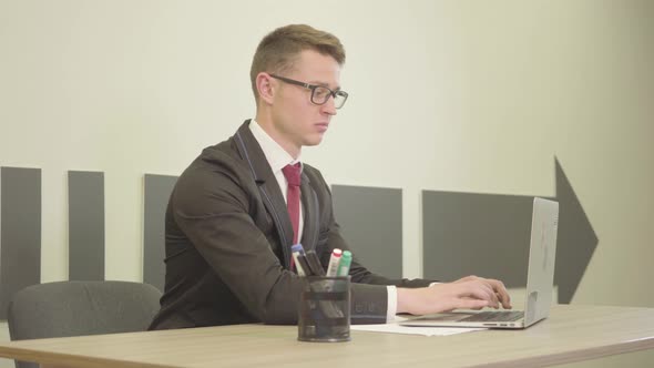 Portrait Young Handsome Man in Formal Wear and Glasses Typing on a Laptop and Showing Thumb Up