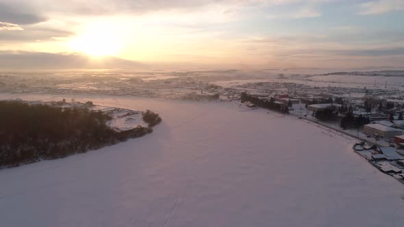 Aerial Orbital Shot of the Frozen Snow Covered Winding River Surrounded with a Little Village on a