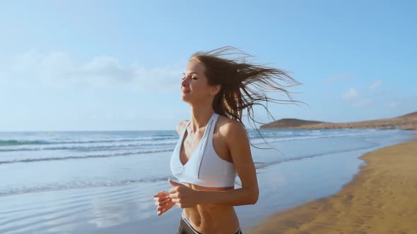 Beautiful Woman in Sports Shorts and T-shirt Running on the Beach with White Sand and Blue Ocean