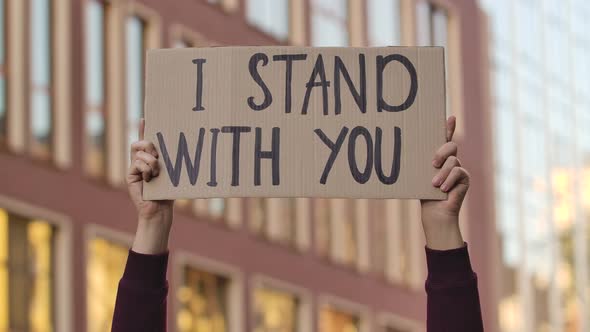 Male Hands Hold a Poster with the Slogan I STAND WITH YOU Against the Background of the City