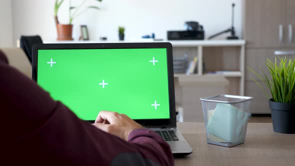 Back Shot of Man Working on a Laptop with Green Screen on It