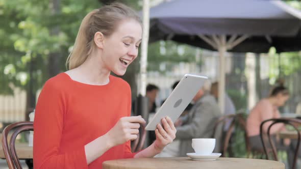 Young Woman Celebrating Win on Tablet Sitting in Cafe Terrace