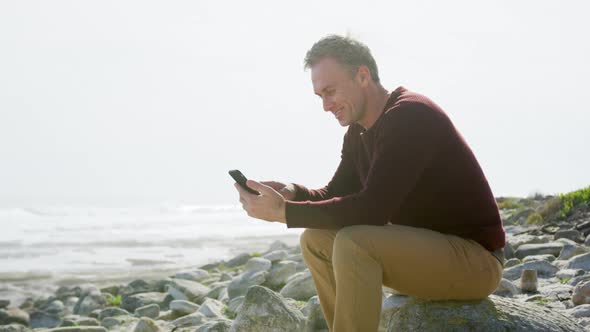 Caucasian man enjoying free time by sea on sunny day sitting on smartphone