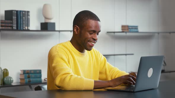 Smiling man typing on laptop keyboard at work desk at home