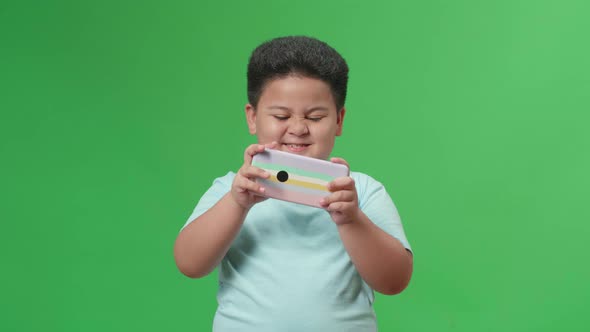 Excited Asian Little Boy Playing Video Game With Mobile Phone In Green Screen Studio