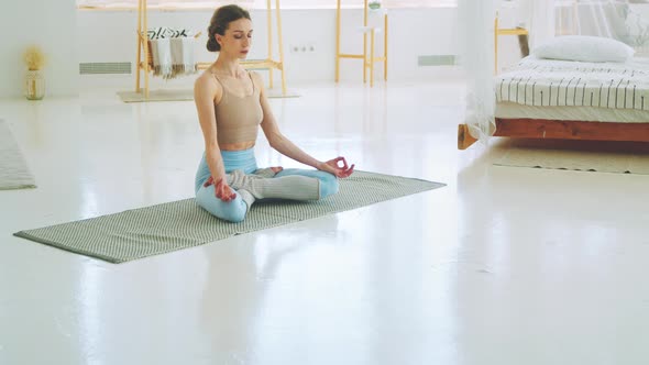 Attractive sportive girl sitting in lotus position. Young girl doing yoga with closed eyes at home