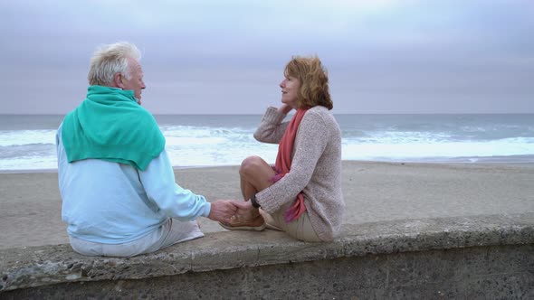 Senior couple sitting on wall at beach together