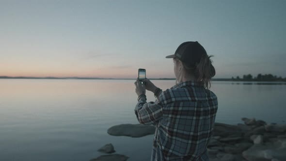 Woman Photographing Sunset over Lake with Smartphone