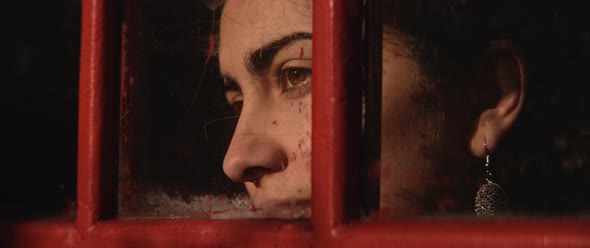 Close up of the eyes of a young woman through a phone booth window