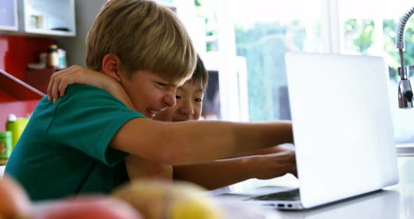 Siblings using laptop in kitchen