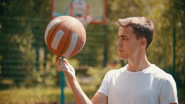 A Young Handsome Man Standing on a Sports Ground and Spinning the Basketball Ball on His Finger