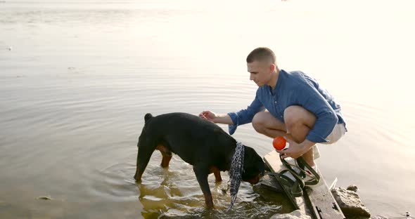 Young Man Playing with Dog Standing on Lake