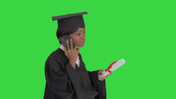 African American Female Student in Graduation Robe Talking on the Phone While Walking on a Green