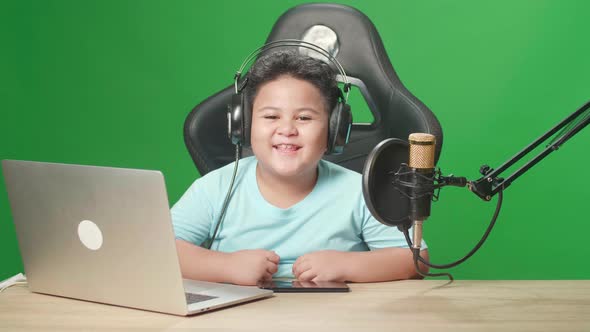 Asian Little Boy Holding Mobile Phone And Smiles To Camera While Live Stream On Green Screen