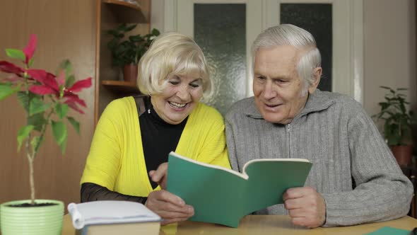 Happy Old Grandparents Couple Sit on Table at Home Enjoy Reading Book Together