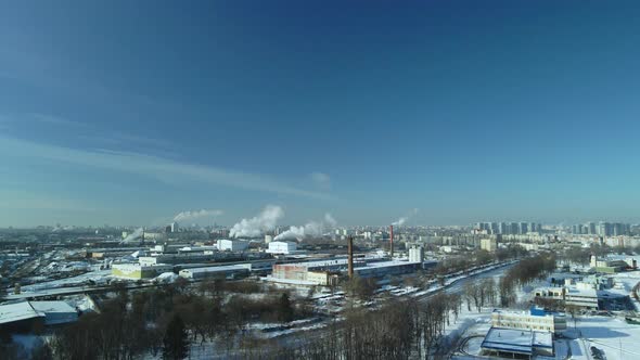 Factory buildings covered with snow. Factory smoke chimneys. There is a railway nearby.