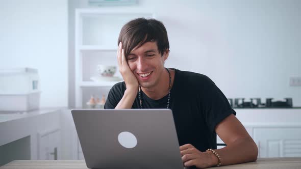 Young Happy Man Looking at Laptop Monitor and Laughing While Reading Funny News While Sitting at