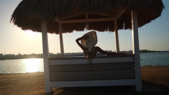 Woman sitting at Cabana with straw roof on a sandy beach on sunset