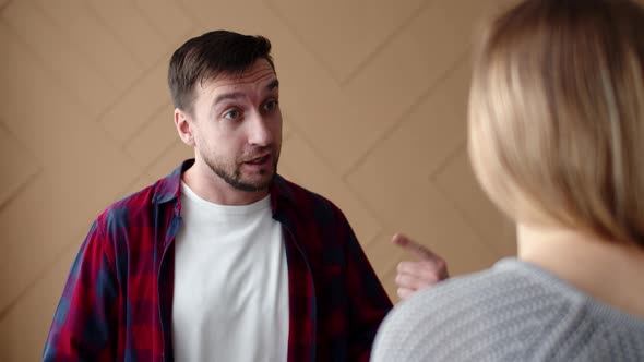 Man swears and shouts at woman emotionally gesturing with hands in bedroom, front view.