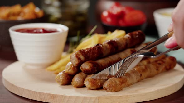 Taking Smoked Sausages with Fork and Cutting Fried Potatoes and Sauce Closeup