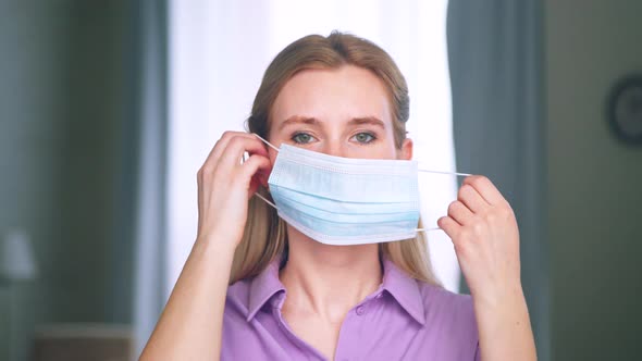 Young girl putting on a blue medical mask in an apartment