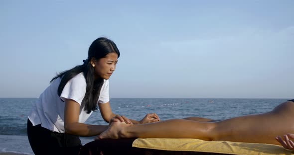 Close-up Massage on the Beach on a Special Table. Asian Masseuse Massages the Whole Legs, Buttocks