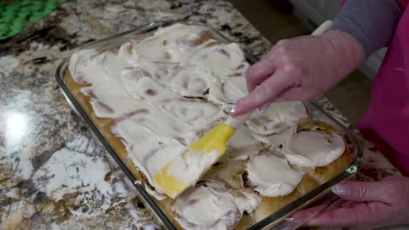 Spreading cream cheese frosting on homemade cinnamon rolls