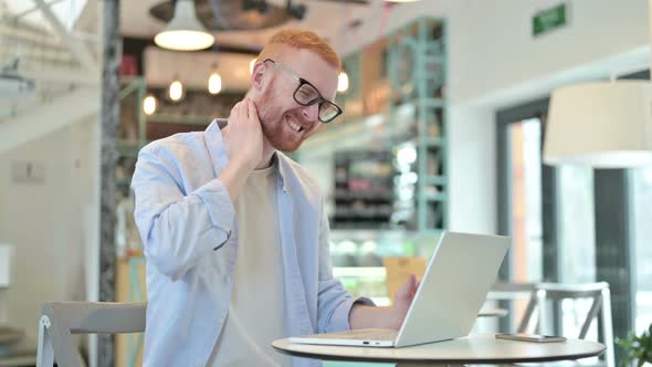 Redhead Man with Neck Pain Using Laptop in Cafe