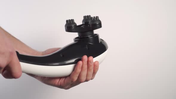 A young man knocks on his hand with a black white electric vibro massager with a raised nozzle. 