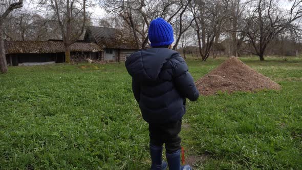 Boy Child in a Blue Hat Walks Through the Yard