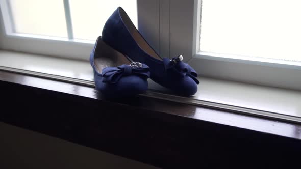 Slow push in shot of a bride's wedding shoes in a large window sill with the rings resting on top