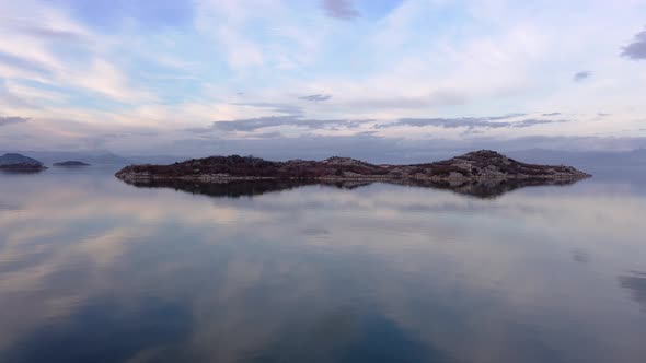 Slow motion of Lake Skadar with crystal clear water reflecting the cloudy sky and beautiful green is