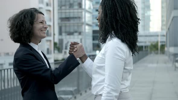 Two Laughing Women Shaking Hands on Street.