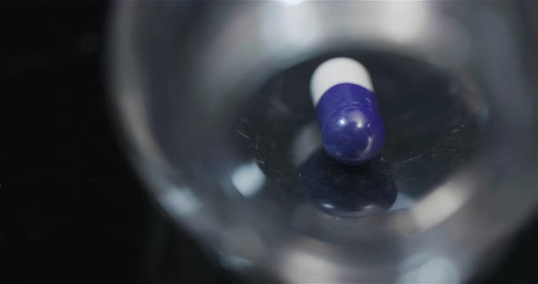 Single Medical Pill in Small Bottle Rotating on Black Background