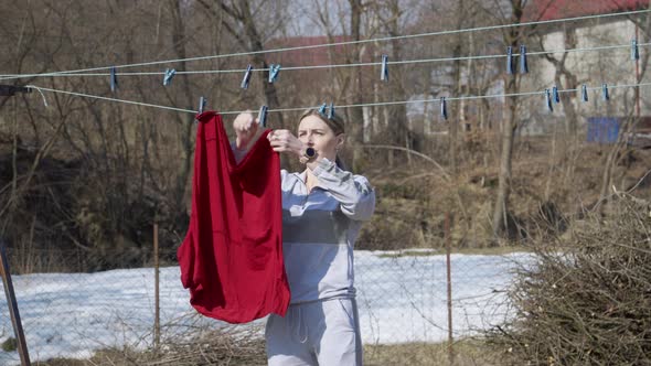 A Young Woman Housewife Hangs Up the Laundry in the Backyard of the House