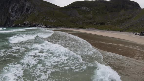 Flying over the ocean and the waves breaking at a beach (Kvalvika beach, Norway) overlooking the mou