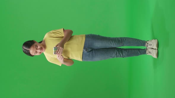 Full Body Of Smiling Young Asian Kid Girl Using Mobile Phone In Green Screen Studio