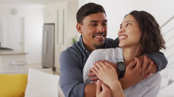 Portrait of happy romantic hispanic couple embracing in living room