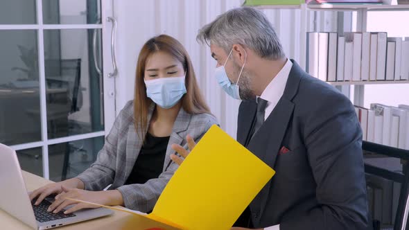 Professional Senior Caucasian boss explaining work to young Asian woman. Indoors, business concept.