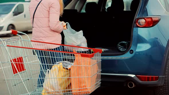 Puts Bags In Trunk Of Car In Mall Parking Lot. Woman Putting Shopping Bags Inside Trunk Supermarket.