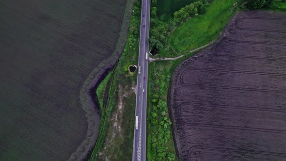 Cars Driving Along the Rustic Asphalt Road Between Fields