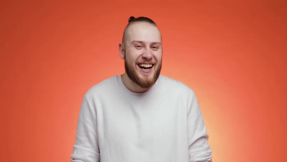 Portrait of Bearded Man with Hair in Tail Is Laughing on Red Background