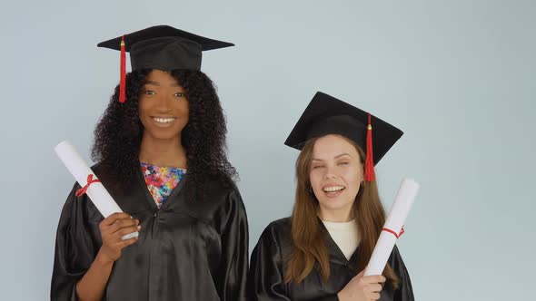 Young African American and Caucasian Women Stand on Side By Side and Hold Educational Diplomas