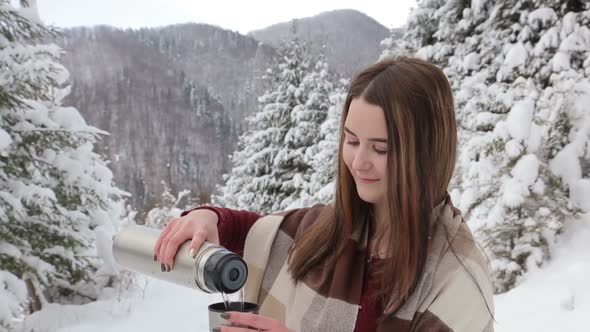 A Young Girl is Drinking Hot Tea in a Snowy Forest She is Warmed By a Drink From a Thermos