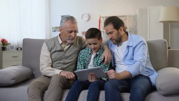 Happy Smiling Grandpa, Dad and Son Scrolling Tablet, Viewing Photos Together