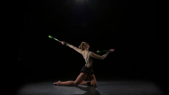 Girl Gymnast with Mace in Hand Revolve Around Him. Black Background