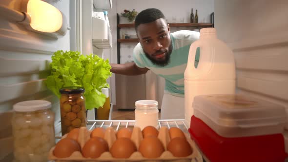 African Male Taking Bottle of Milk From Full Fridge