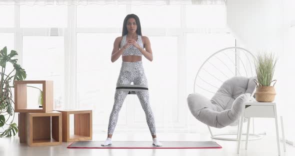 Athletic African American beautiful woman doing squat using a fitness elastic band.