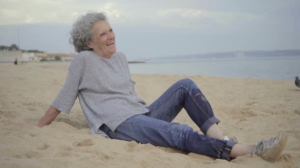 Beautiful Elderly Woman Sitting on Sand and Laughing